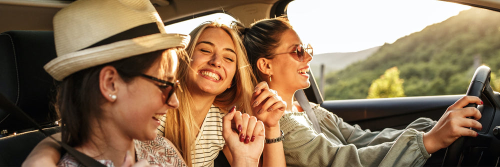 Three people smiling and holding hands in a car, with green hills visible outside the window.