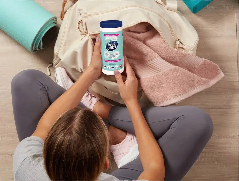 A person holding Wet Ones Lavender wipes near a gym bag on a wooden floor with a yoga mat.