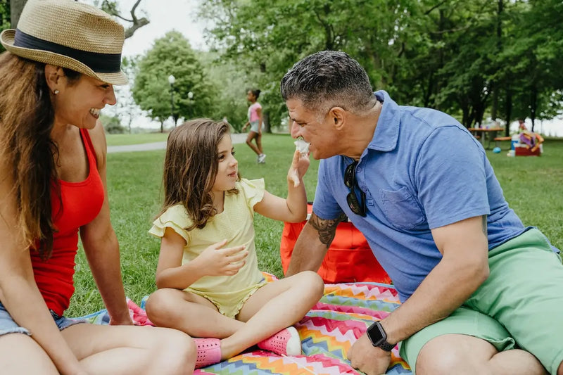 Family enjoying a picnic in the park, sitting on a colorful blanket and sharing laughter outdoors.